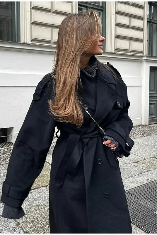 Black double-breasted trench coat with belt at waist, stylish Lumina Wear Cheri trench coat, shown on a model.