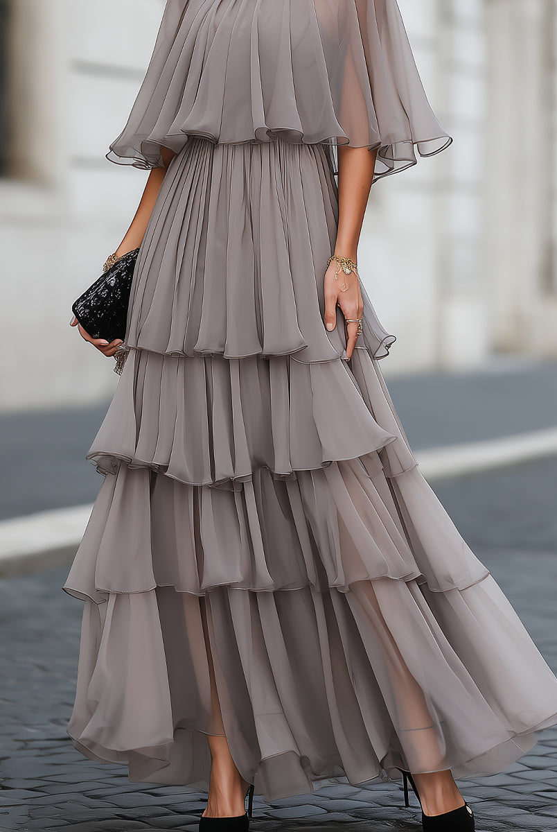 Elegant tiered pleated maxi dress with sheer cape overlay by Lumina Wear, shown on a model with flowing fabric and detailed design.