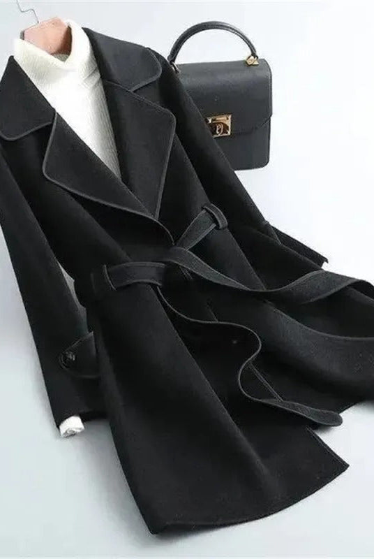 Black Verona trench coat by Lumina Wear featuring elegant design and contrast piping, shown hanging on a wooden door.