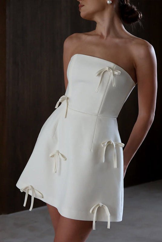 White satin strapless mini dress with bow accents from Lumina Wear's Sidonie collection, featuring a fitted silhouette and elegant design.