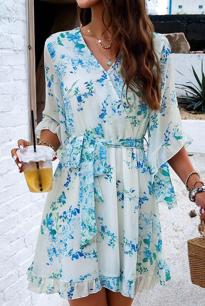 Lumina Wear Alba women's floral V-neck mini dress displayed on a model, featuring a white fabric and feminine ruffle details.