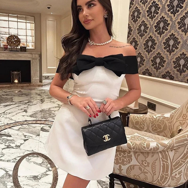 White Nova off-shoulder mini dress with bow detail, by Lumina Vancouver, featuring a chic, feminine style perfect for summer wear.