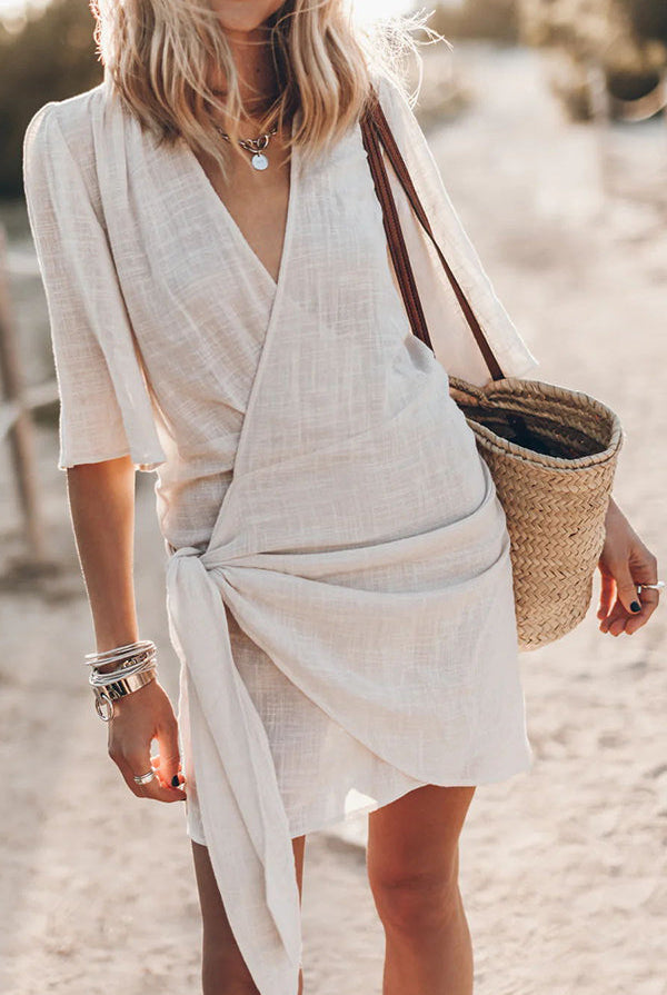 Yellow Nova Wrap Mini Dress by Lumina Wear, made of cotton and linen, shown on a model in a casual outdoor setting.