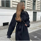 Black double-breasted trench coat with belt at waist, stylish Lumina Wear Cheri trench coat, shown on a model.