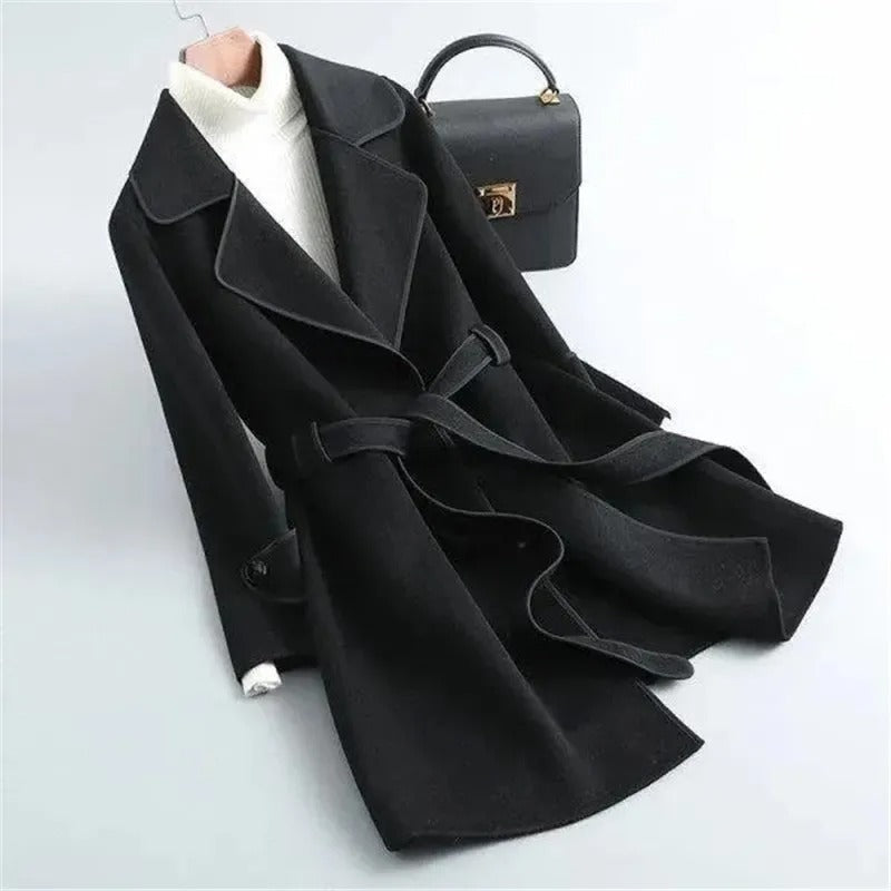 Black Verona trench coat by Lumina Wear featuring elegant design and contrast piping, shown hanging on a wooden door.