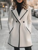 Lumina Wear double-breasted white coat with black trim, stylish coat for women, shown on a model with a modern urban background.
