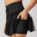 Light brown Isabella elegant pleated mini skirt with integrated shorts from Lumina Wear, shown on a model.