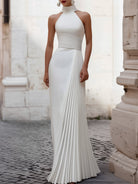 White Isabelle pleated halter-neck gown by Lumina Wear, elegant floor-length dress with a fitted waist and flowing skirt.