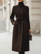 Brown Lumina Vancouver Georgie belted wool blend maxi coat hanging on a wooden hanger, showcasing its length and tailored fit.