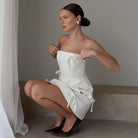 White satin strapless mini dress with bow accents by Lumina Vancouver, featuring a fitted silhouette and elegant design.
