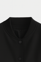 Elegant black bomber jacket from Lumina Wear featuring a timeless design, shown on a model with a modern urban background.